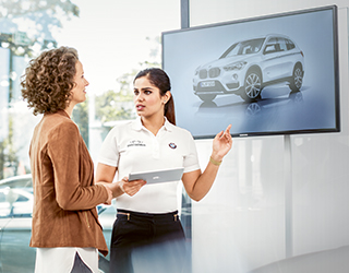 Women talking infront of a screen showing a car (photo)